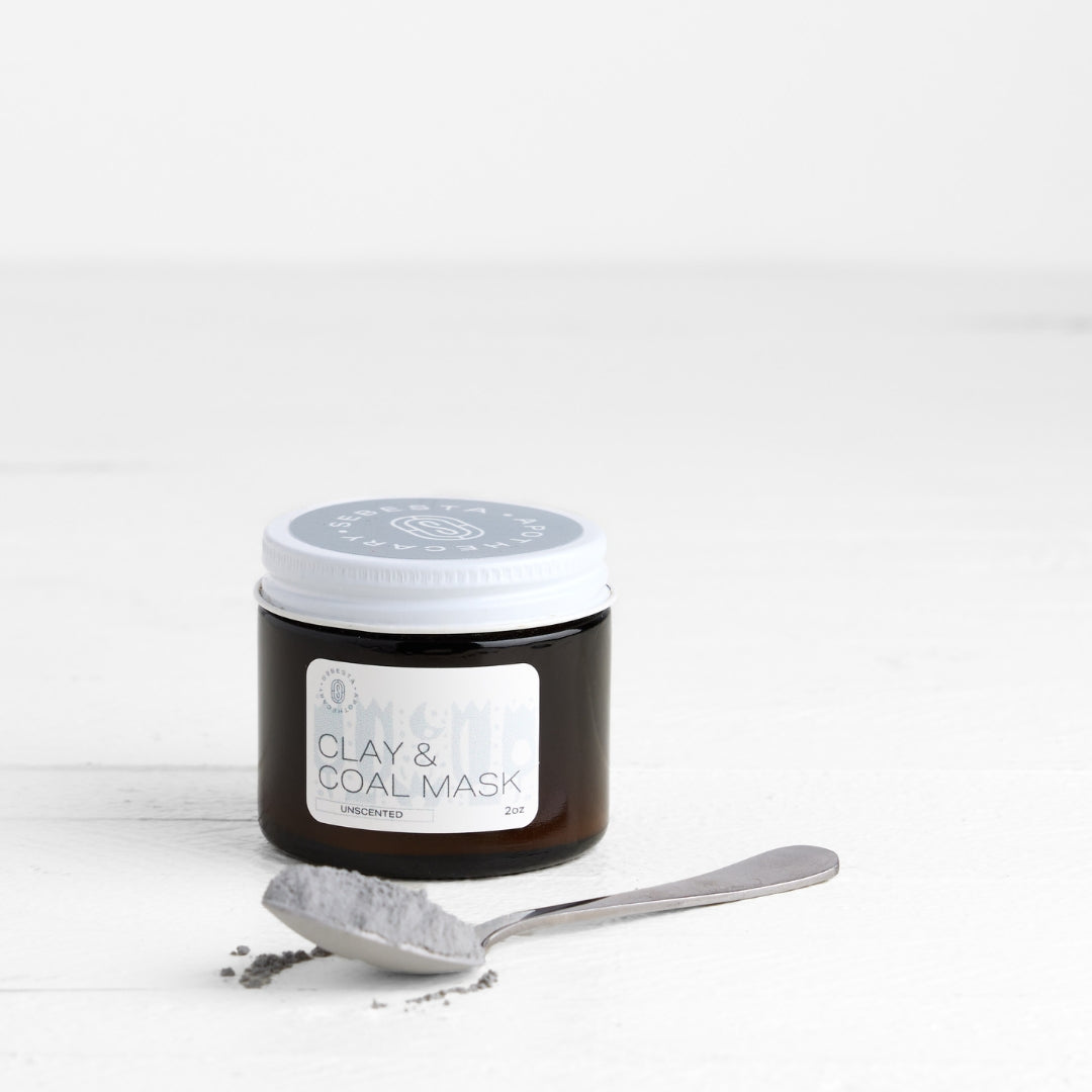 Jar of clay and coal mask with a spoon on a white background
