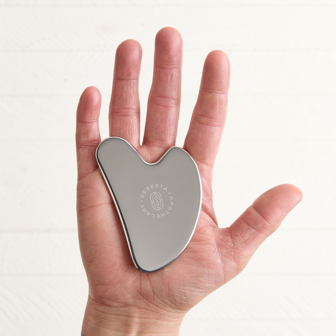 Stainless steel Gua Sha with Sebesta Apothecary Logo in hand white background