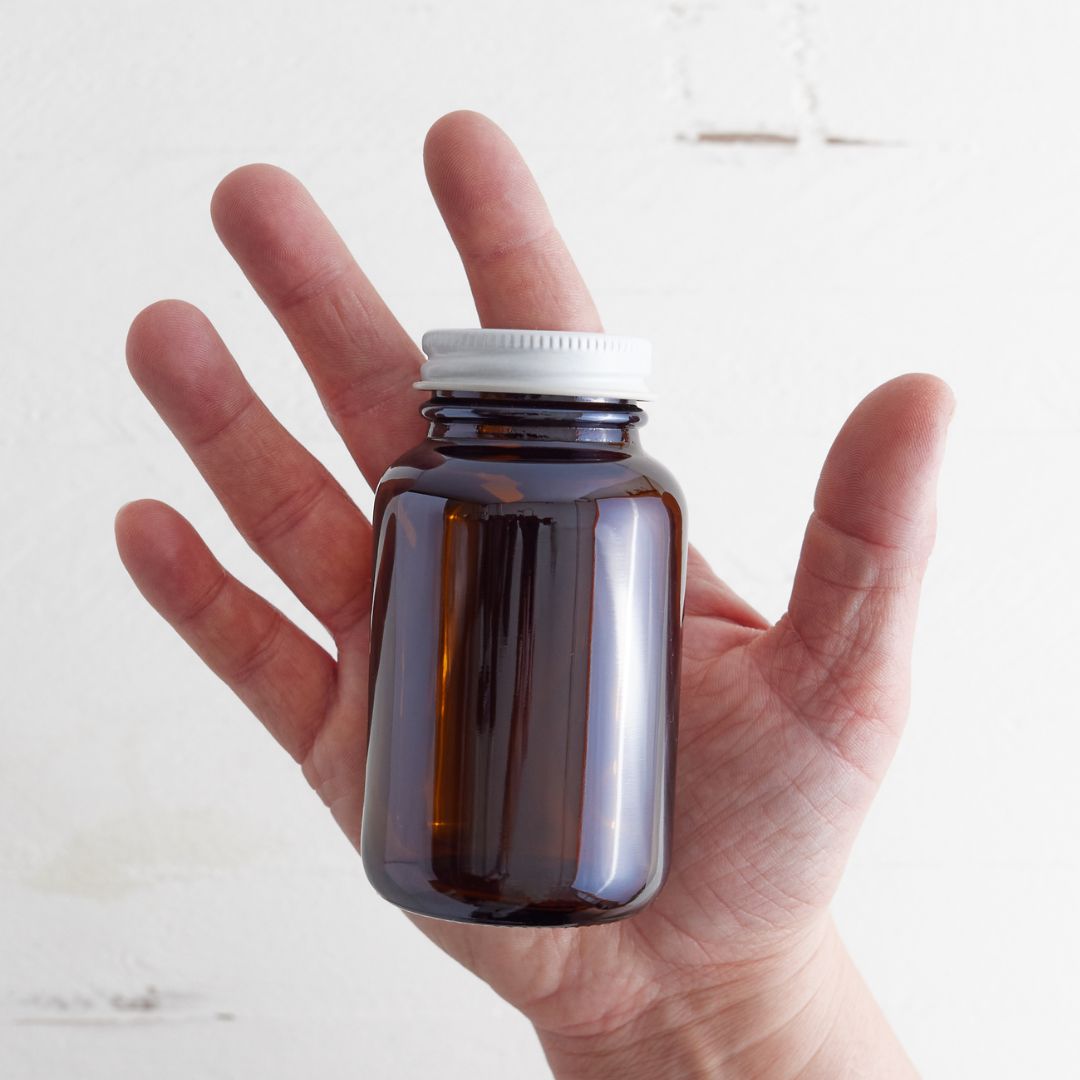 Sebesta Apothecary 4oz Amber Glass jar with white metal lid in hand with white background