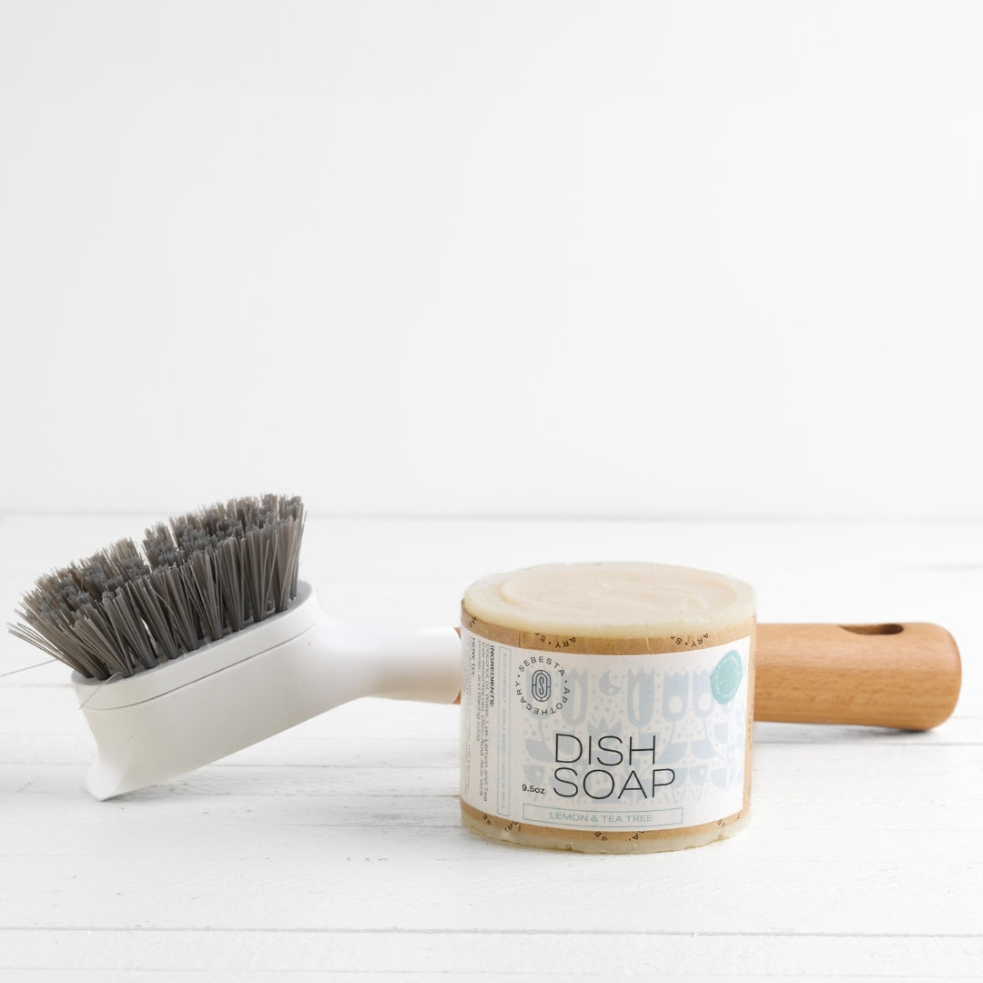 large cylinder bar of soap with Sebesta Apothecary Branding on white background. Dish brush in background