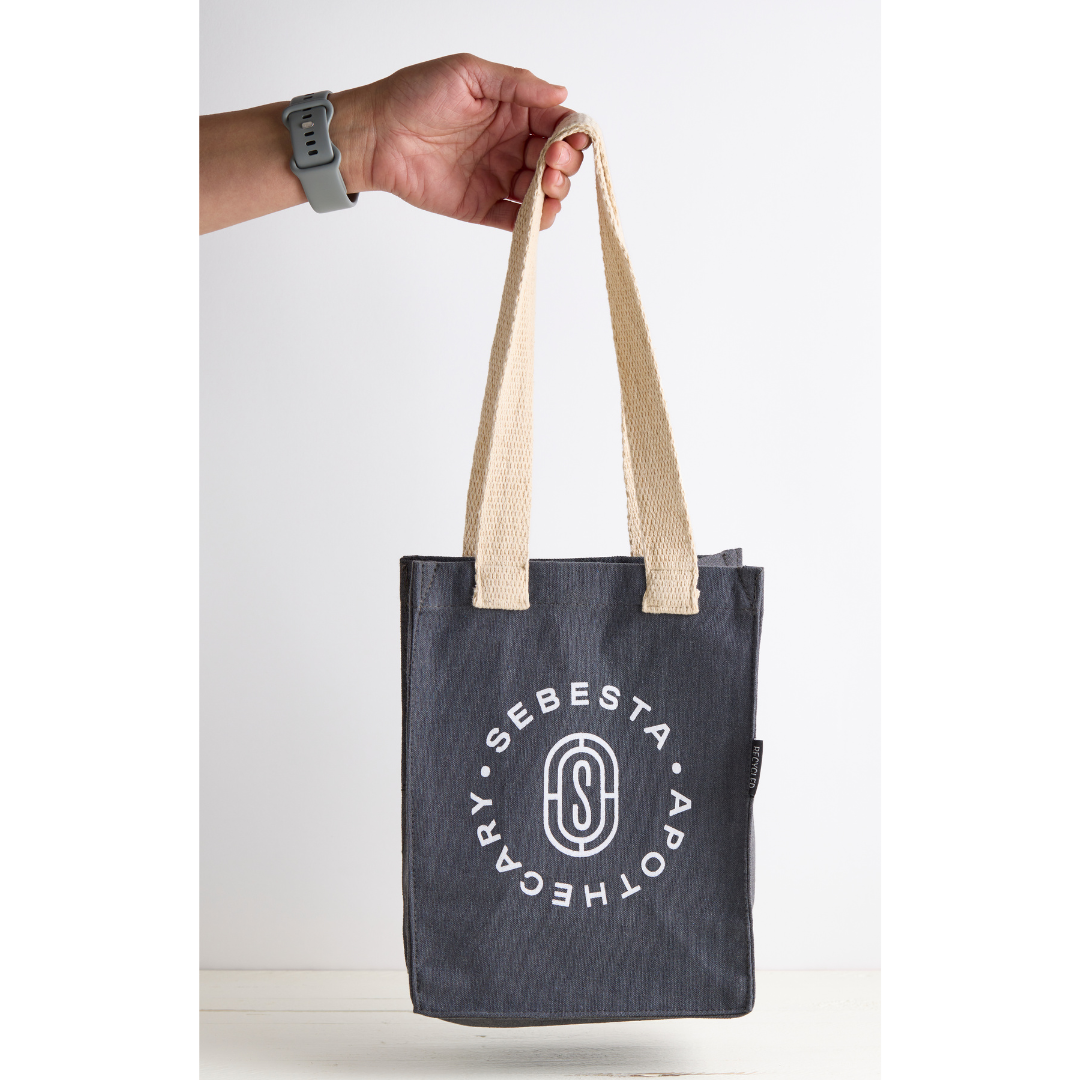 Tote bag with 'Sebesta Apothecary' logo held by a hand on a white background