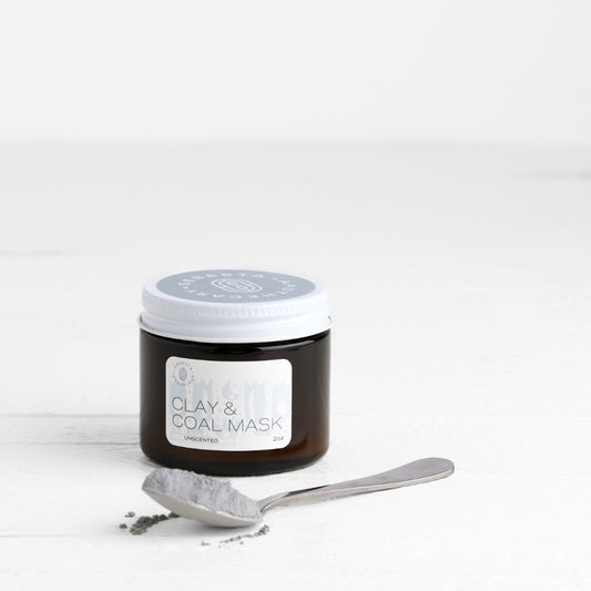 Jar of clay and coal mask with a spoon on a white background