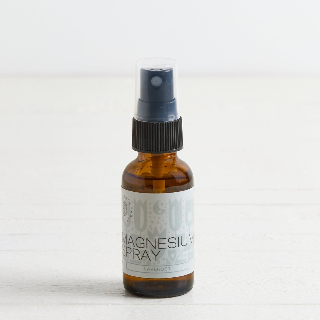 An amber glass spray bottle of Magnesium Spray with a black pump and a white label, set against a light, neutral background.