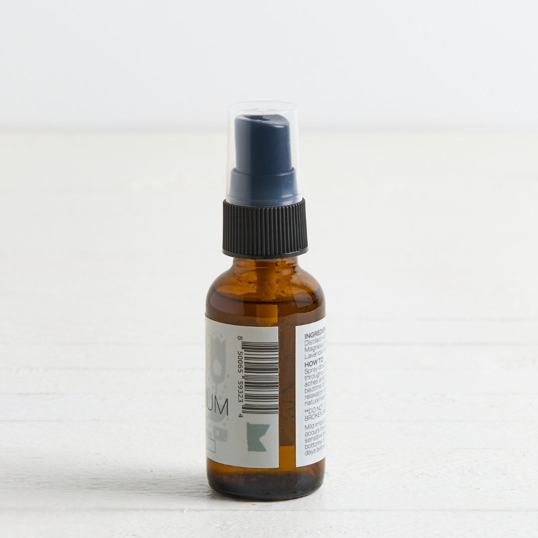An amber glass spray bottle with a black ribbed collar and a clear protective cap on the nozzle, standing on a white surface against a white background.