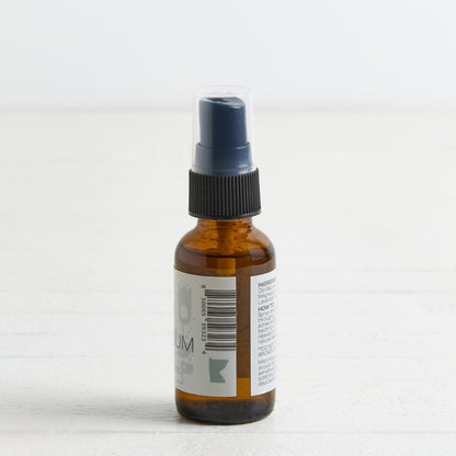 An amber glass spray bottle with a black ribbed collar and a clear protective cap on the nozzle, standing on a white surface against a white background.