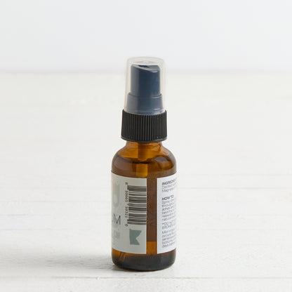 An amber glass spray bottle with a black spray nozzle and a clear protective cap, shown from the back with a white label on a light background.