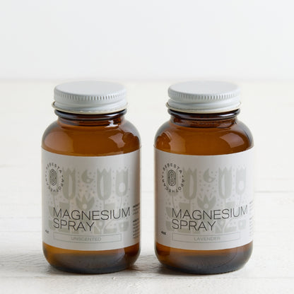 Two amber glass bottles of Magnesium Spray, one unscented and one lavender, with white labels and white caps, set against a clean white background.