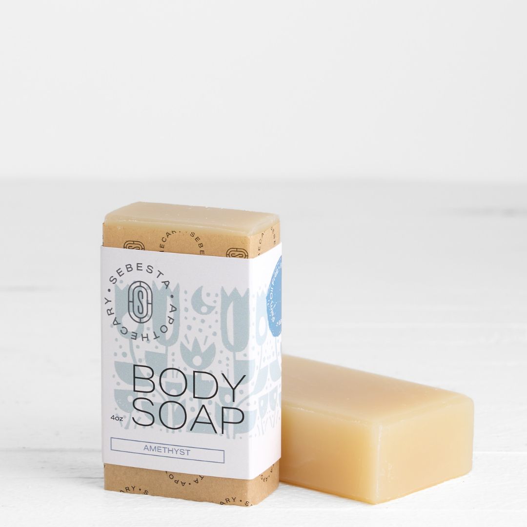 Bar of soap with paper wrapped standing up and plain bar of soap laying down on a white background
