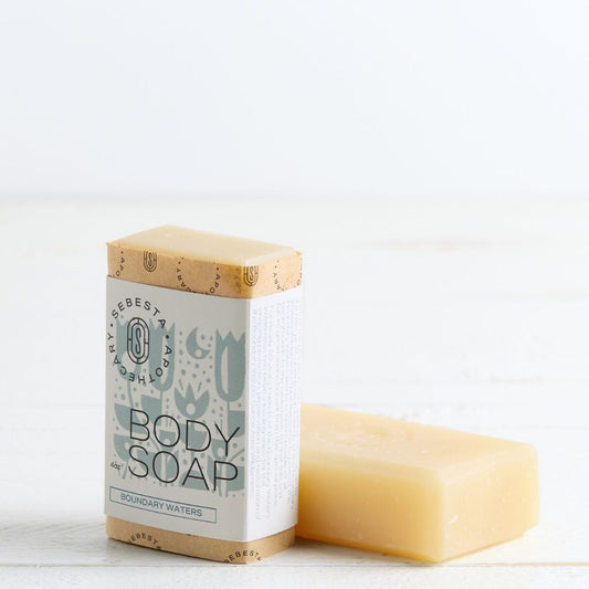 Sebesta Apothecary Soap bars - one standing with label facing forward the other unlabeled on table. White background and table
