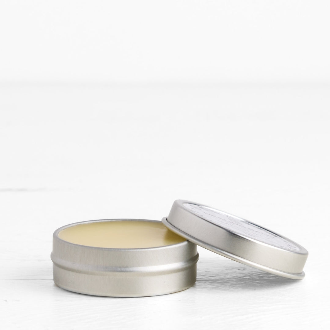 Metal tin with balm in it. Open lid, off to the right side. White background