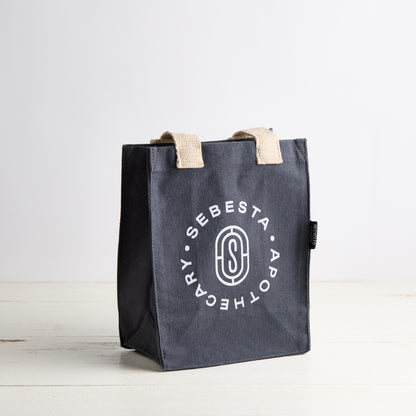 Black tote bag with 'Sebesta Apothecary' branding on a white background