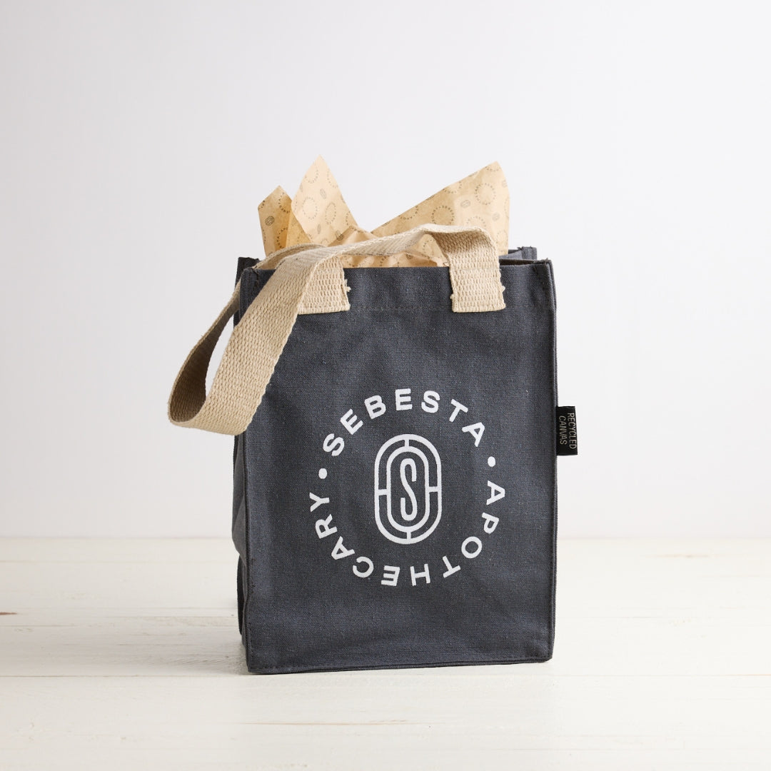 Black tote bag with 'Sebesta Apothecary' logo on a white background